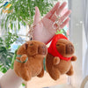 A fluffy brown capybara plush keychain charm with a red knitted hat is held in a person's hand.