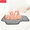 A baby is lying on a gray portable foldable waterproof diaper changing pad on a white bed.