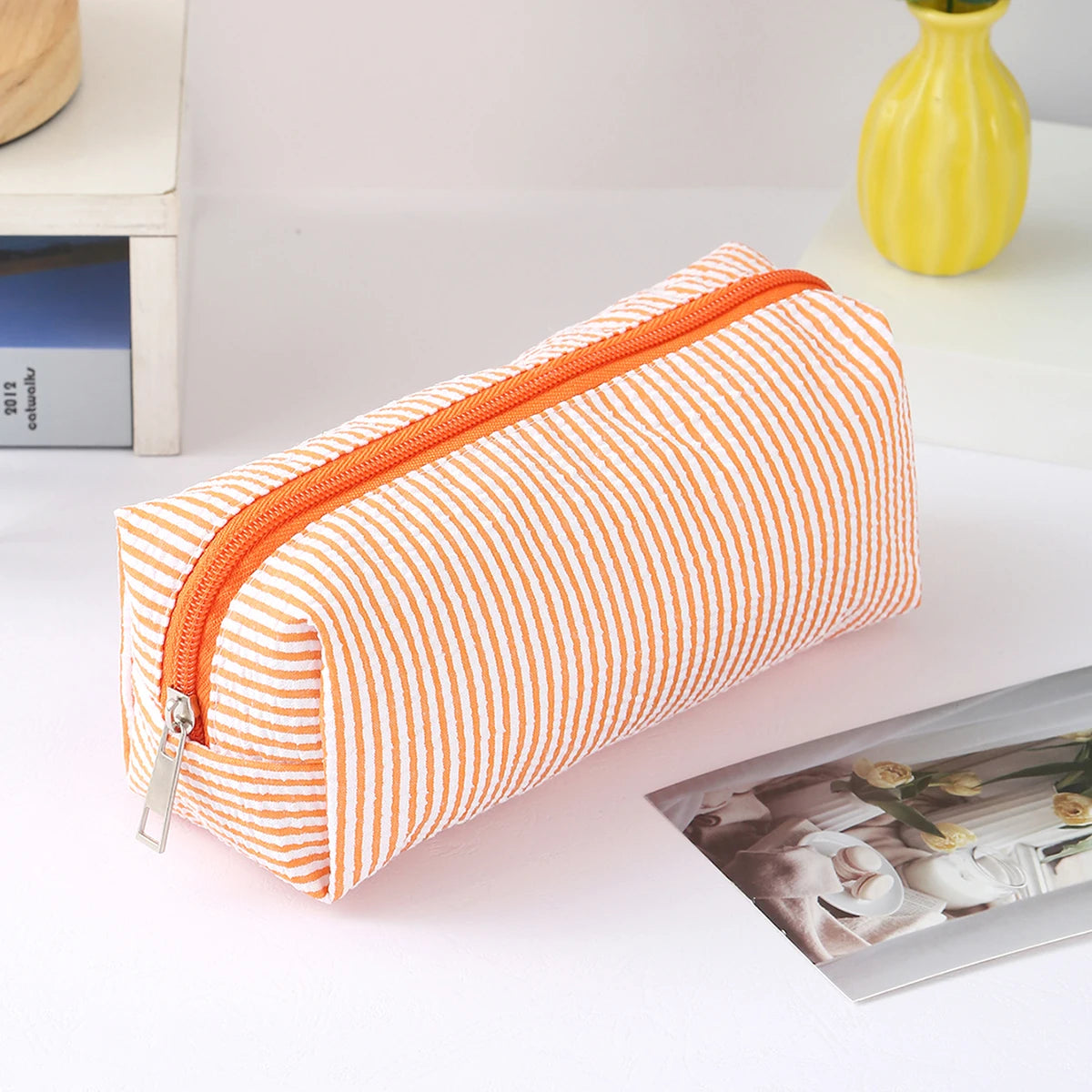 An orange and white striped canvas pencil case with a zipper is shown on a white surface.