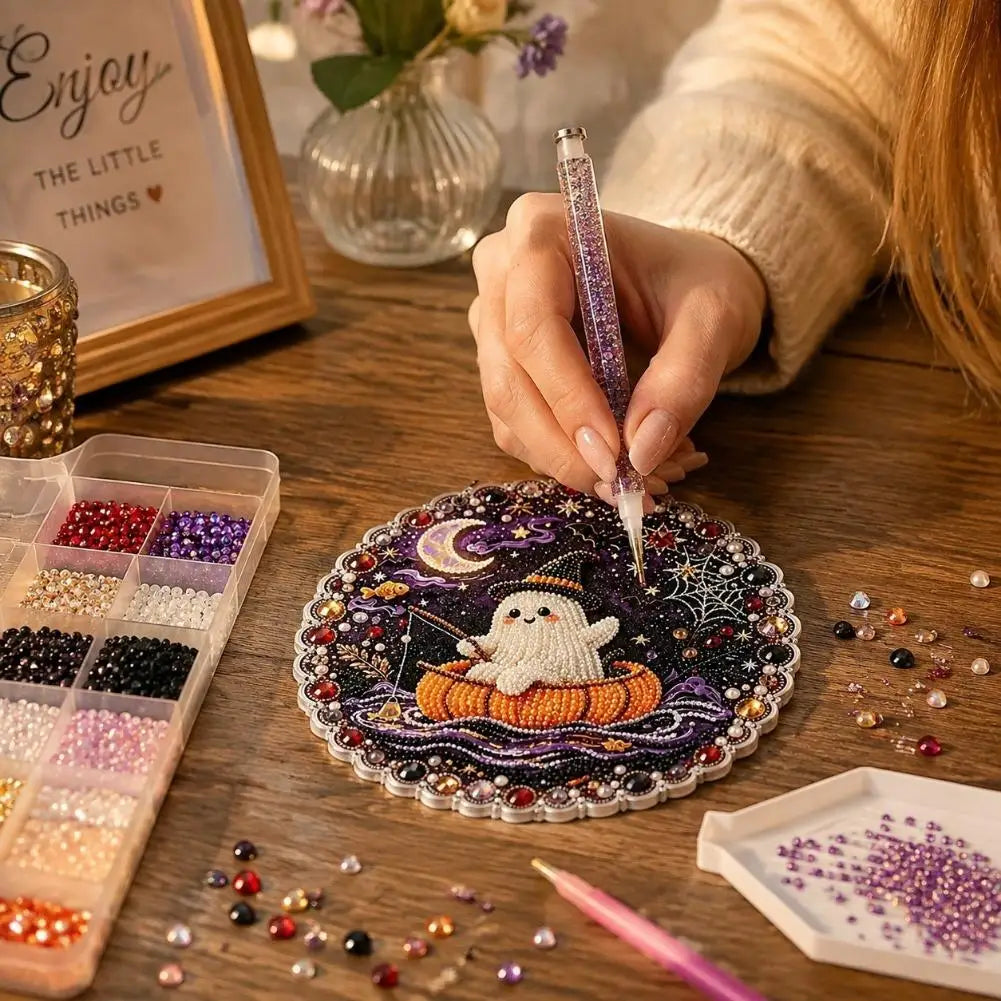 A hand paints a Halloween diamond painting ornament featuring a white ghost on an orange pumpkin amidst scattered glitter and