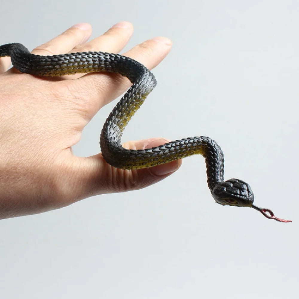 A hand is holding a lifelike rubber snake decoy with mottled black and olive green coloring.