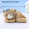 A cute, light brown 3D bear cake topper with a blue bow, shown lying on a white surface.