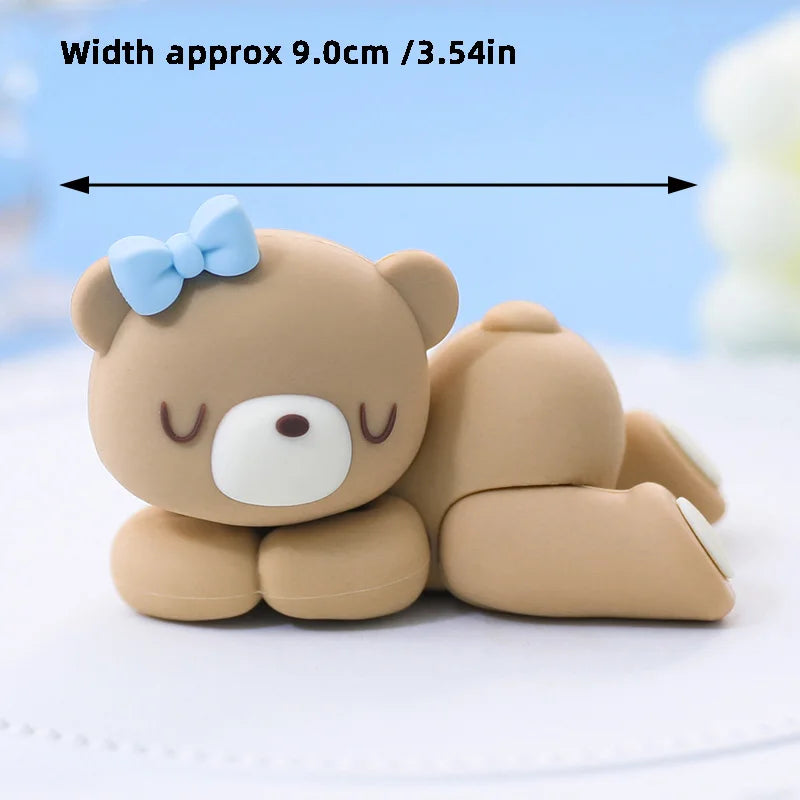 A cute, light brown 3D bear cake topper with a blue bow, shown lying on a white surface.