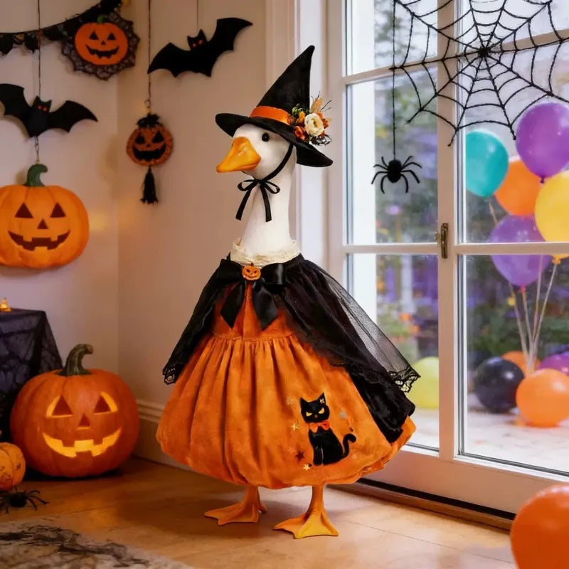 A white goose costume with a black witch hat and orange pumpkin outfit standing in front of a window decorated for Halloween.