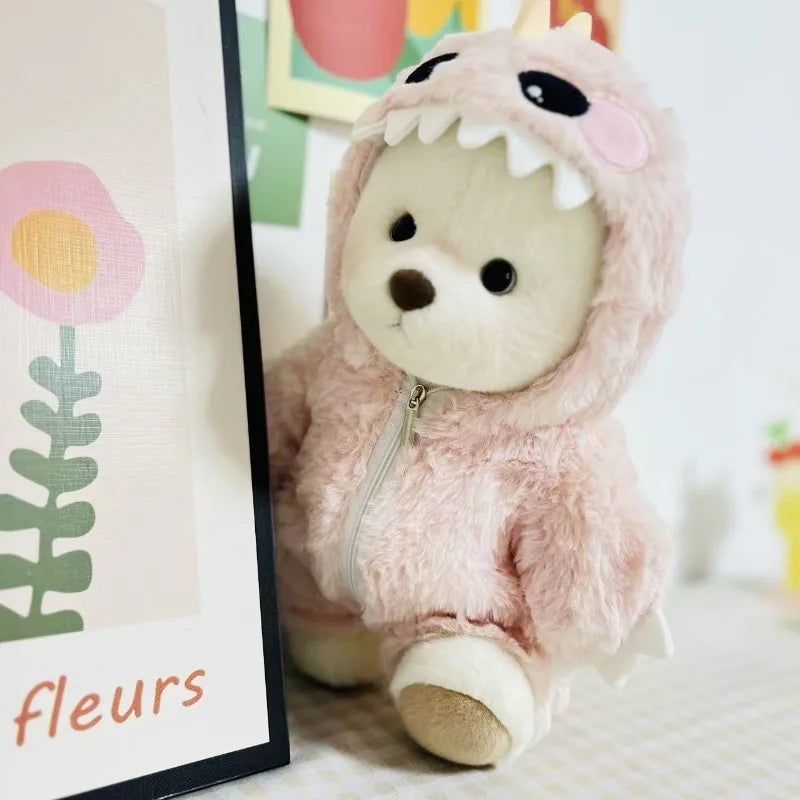 A soft pink plush doll wearing a hood and clothing set, positioned next to a framed floral print.