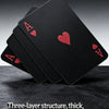 A stack of black playing cards with red aces resting on a dark surface.