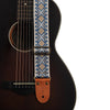 An embroidered guitar strap featuring blue and white geometric patterns with leather ends.