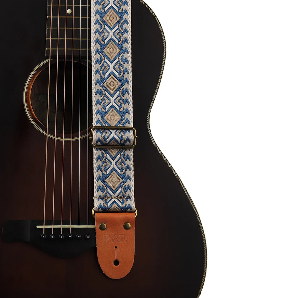 An embroidered guitar strap featuring blue and white geometric patterns with leather ends.