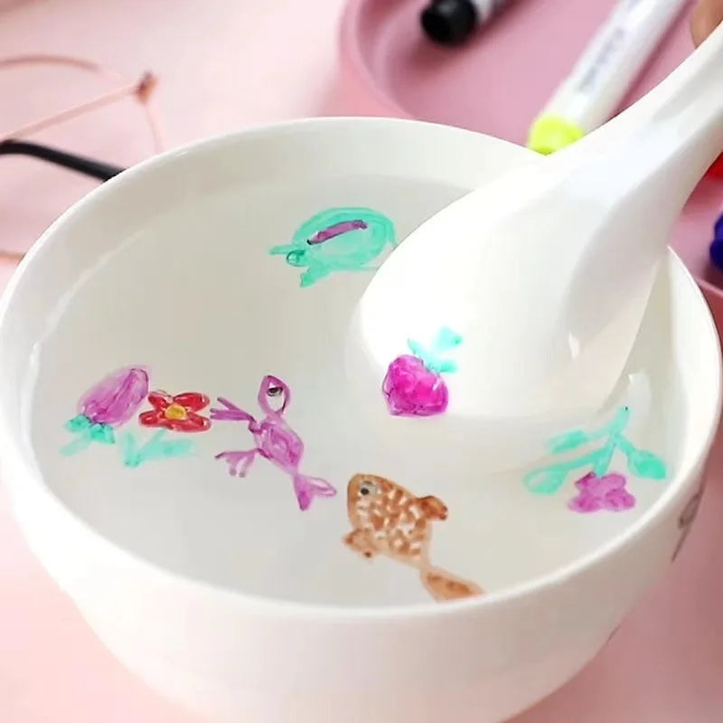 A white ceramic bowl contains colorful ink and a white ceramic spoon, part of a magic floating ink art kit.