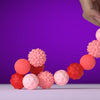 A hand is holding a string of pink and red soft sensory silicone massage balls against a purple background.