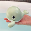 A light green clockwork animal bath toy is held in a hand against a blue background.