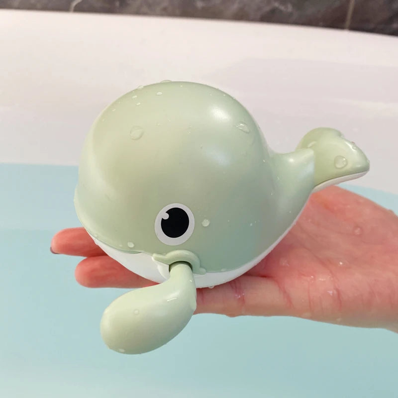 A light green clockwork animal bath toy is held in a hand against a blue background.