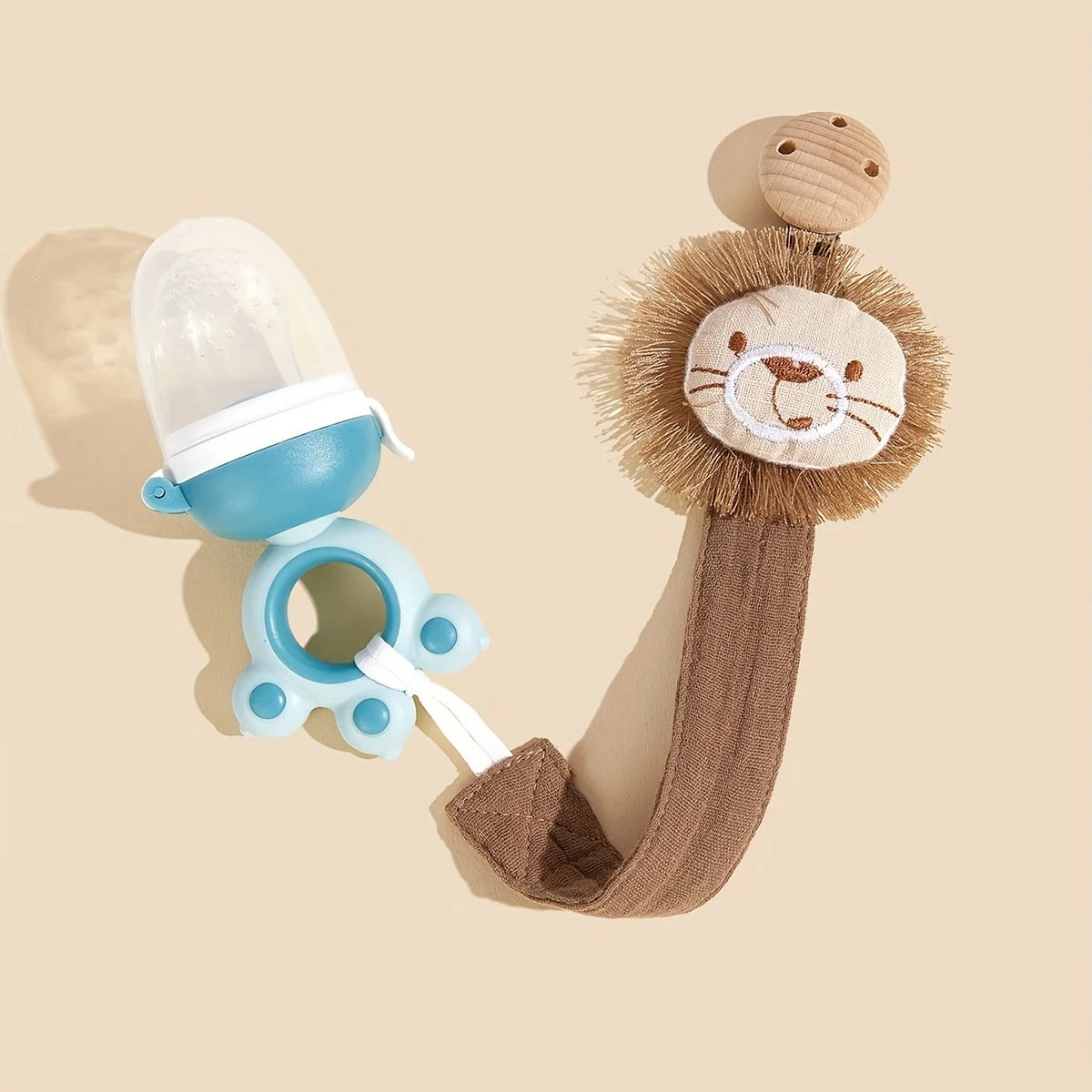 A light blue elephant pacifier holder with a clip and a brown fabric strap is shown against a beige background.