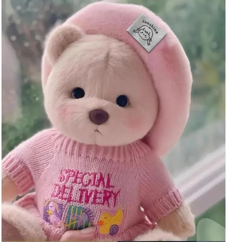 A pink teddy bear plush toy wearing a pink knitted sweater and a pink hood.