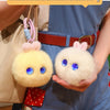 A fluffy white rabbit plush pendant with blue eyes is held by a person wearing a blue apron.