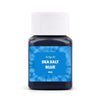 A small glass bottle of Sea Salt Blue textile fabric dye kit with a white cap.