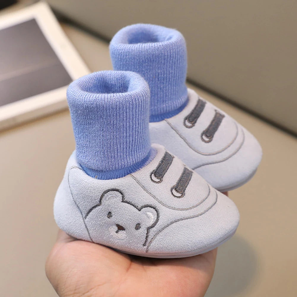 A pair of light blue baby soft sole first walker shoes with knitted cuffs and anti-slip TPR soles being held in a hand.