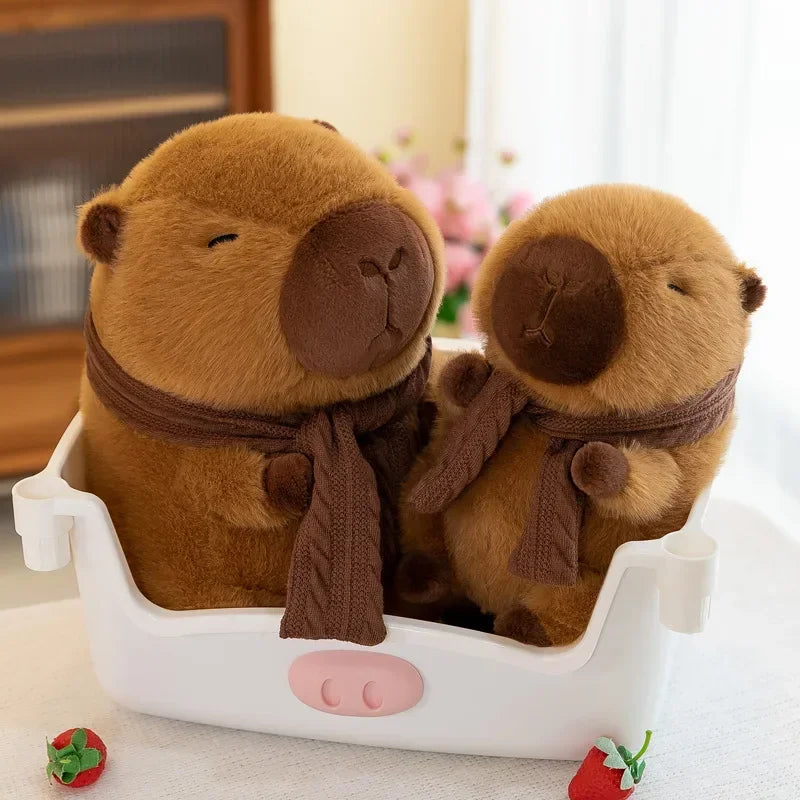 A cute brown plush capybara stuffed animal wearing a knit scarf is displayed in a white container.