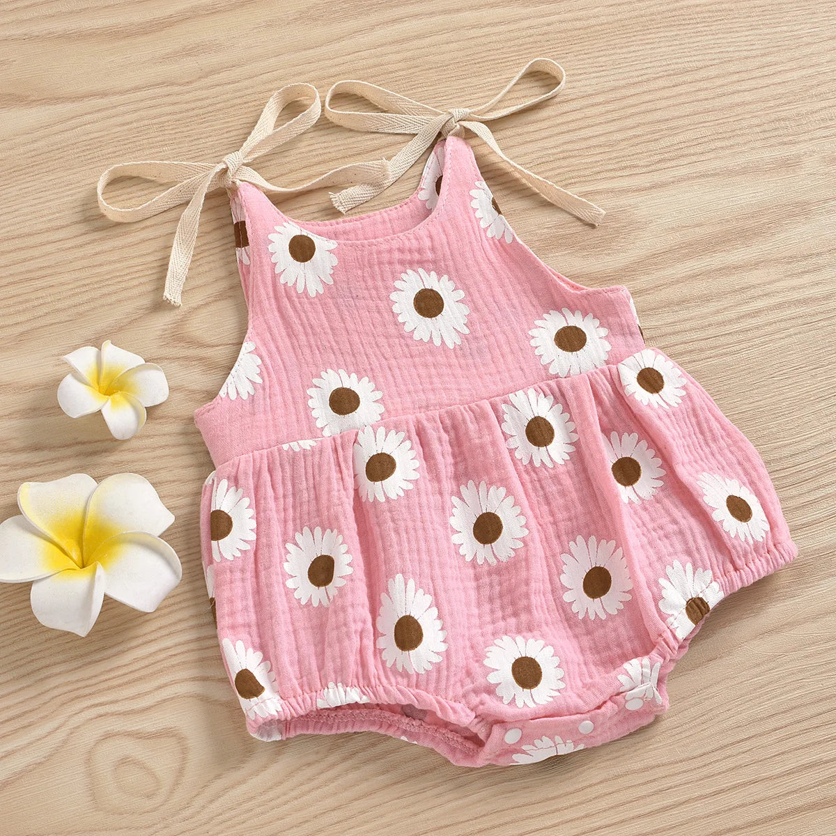 Pink cotton romper for a baby girl with a white daisy floral print and adjustable ties