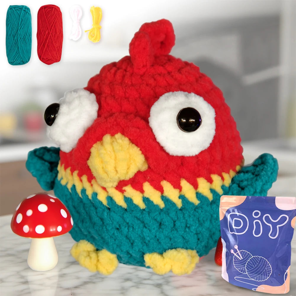 Un jouet d'oiseau tricoté rouge et vert fini, à côté de différents fils et d'un kit DIY.