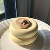 A round, light yellow creamy soufflé with a small, sculpted face on top, resting on a white plate.