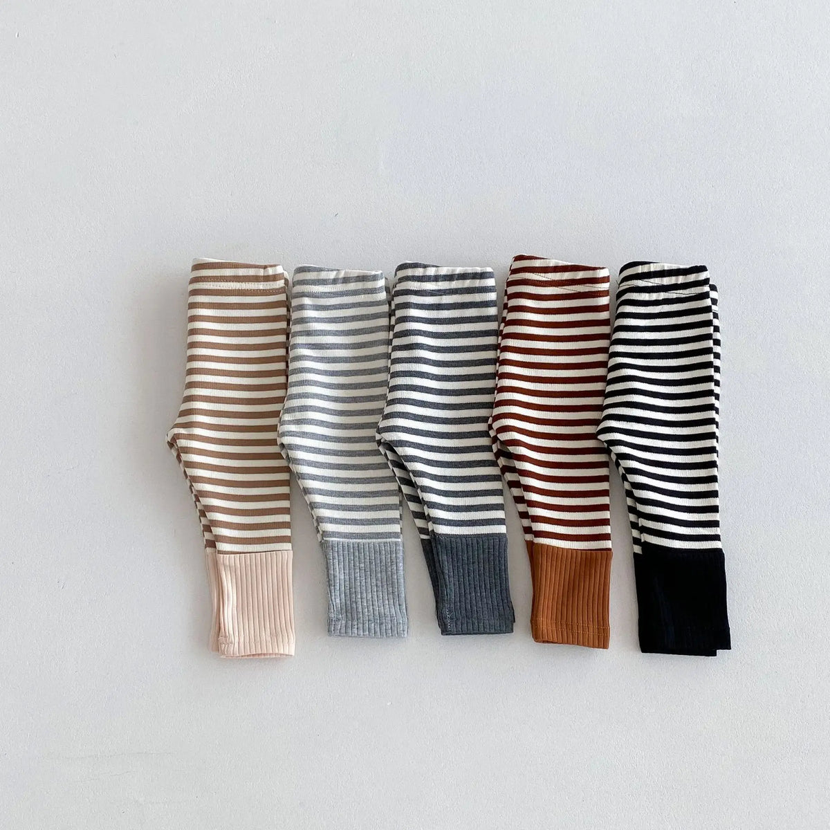 A row of striped baby leggings in brown, gray, and black tones displayed horizontally.