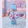 A blue wrist watch with a rainbow design and a light blue strap is displayed in a soft, pastel-colored setting.