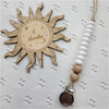 A wooden sun-shaped bead pacifier clip with a silicone teether is displayed on a white textured surface.