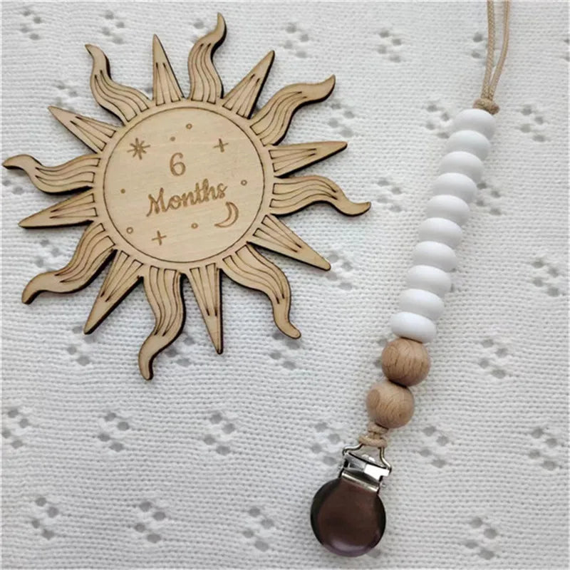 A wooden sun-shaped bead pacifier clip with a silicone teether is displayed on a white textured surface.