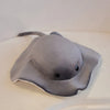 A gray plush toy shaped like a devil fish with a snout and fins resting on a white surface.
