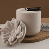 A white ceramic candle cup sits on a beige coaster next to a white floral silicone mold.
