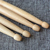 A pair of light wood maple drumsticks lying diagonally on a gray textured surface.