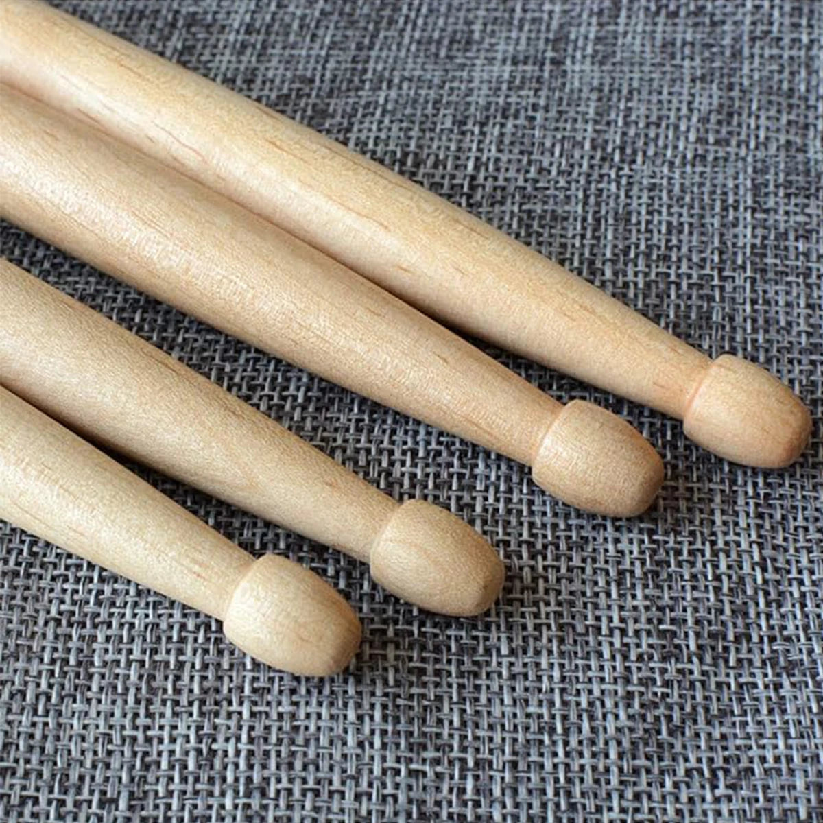 A pair of light wood maple drumsticks lying diagonally on a gray textured surface.