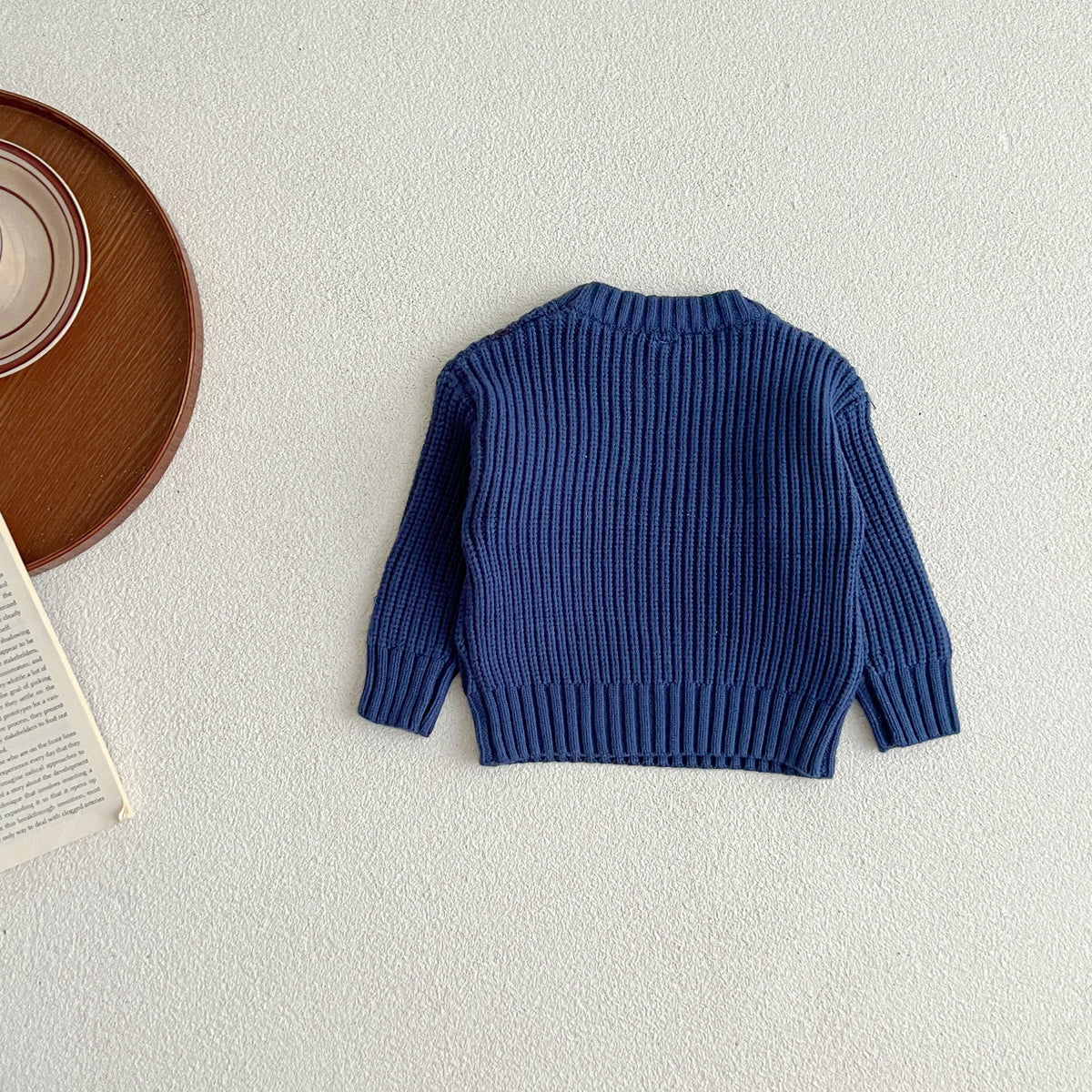 A navy blue ribbed knit baby pullover sweater lying flat on a light surface.