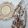A wooden baby pacifier clip featuring silicone beads and a natural fiber wreath with the word hello world.