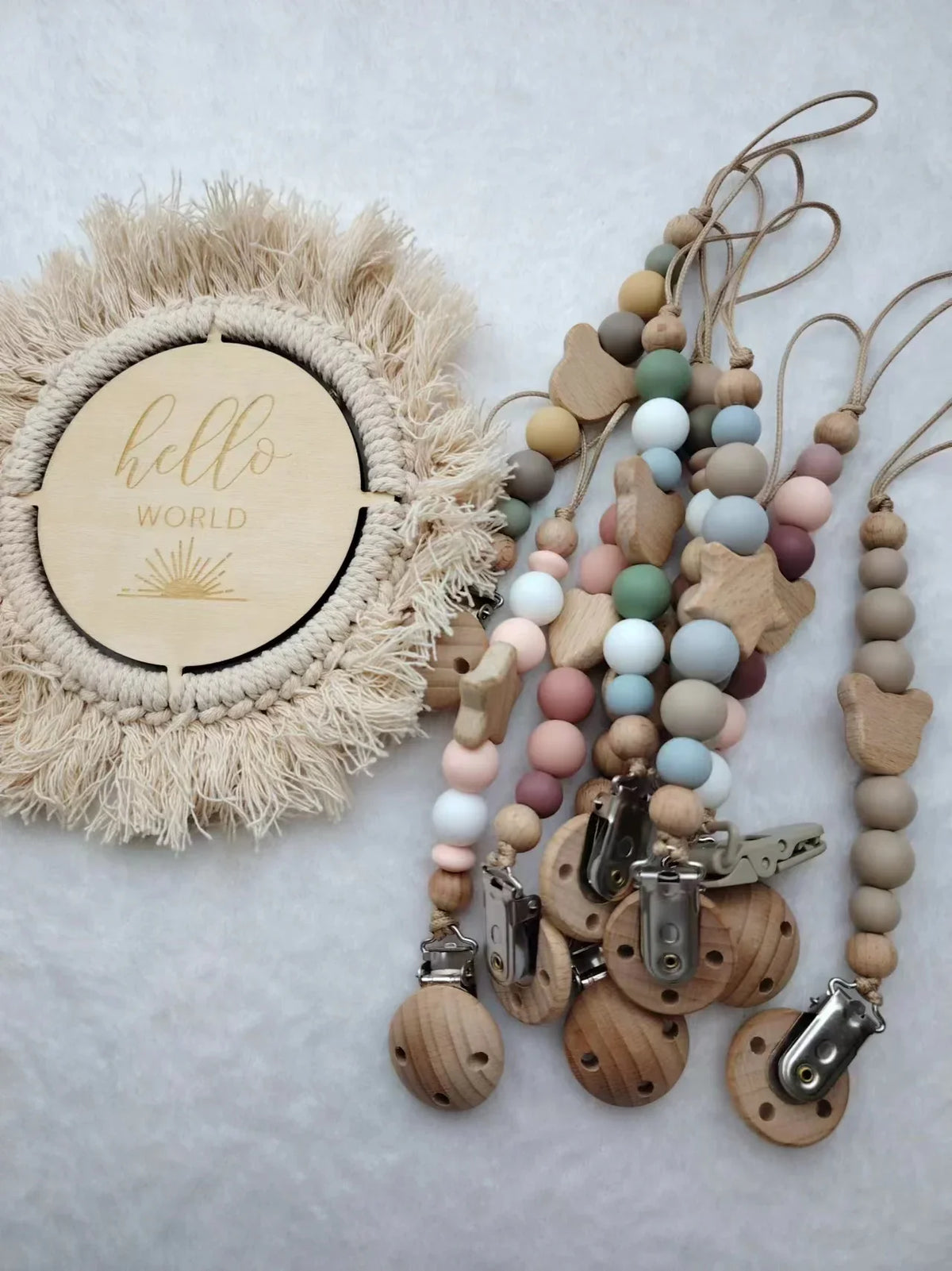 A wooden baby pacifier clip featuring silicone beads and a natural fiber wreath with the word hello world.