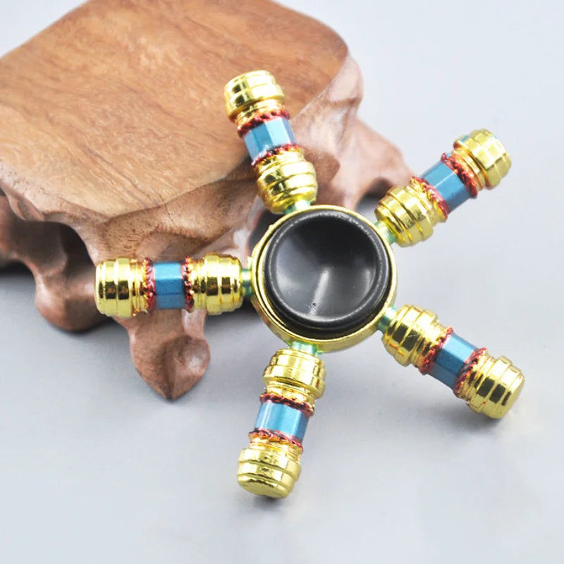 A metal fidget spinner with a rainbow finish is displayed on a wooden surface.