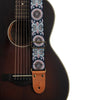 An embroidered guitar strap featuring blue and white patterns with leather ends attached to a dark acoustic guitar neck.