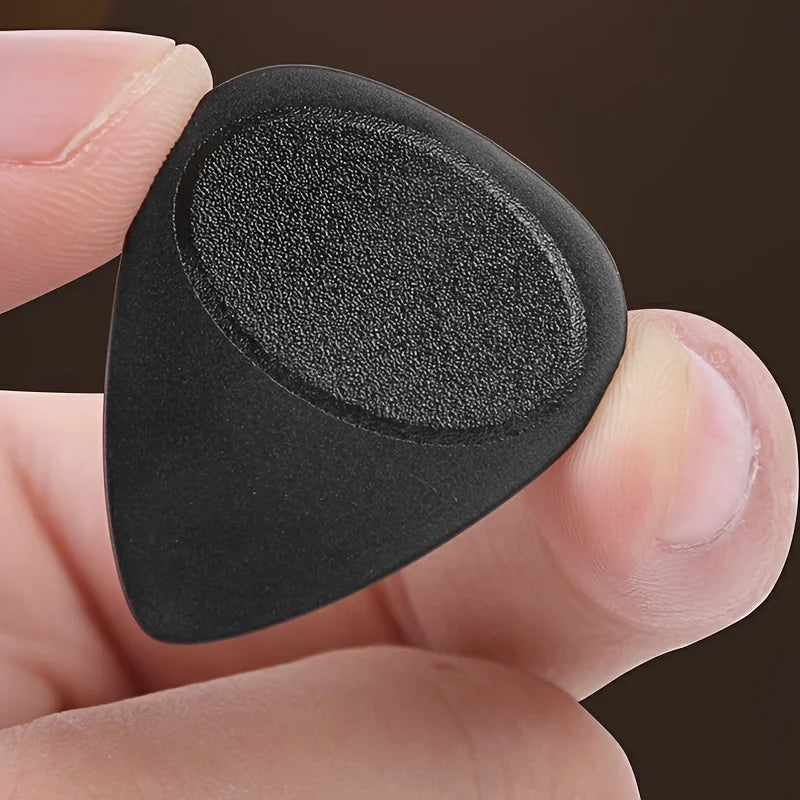 A hand holds a black guitar pick with an anti-slip grip, showing its shape and texture.
