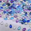A close-up of iridescent water drop Czech glass beads in various shades of blue, purple, and clear white.