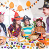 A group of children smiling while holding and interacting with various Halloween squishies and soft toys.