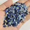 A hand holds a pile of dark blue and light blue tumbled stone chips for jewelry making