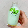 A clear bottle filled with a light green liquid and topped with two green fruit-shaped squishy toys.