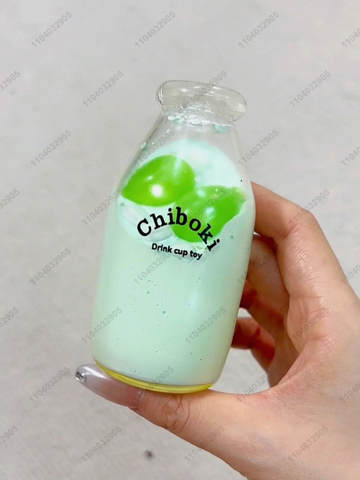 A clear bottle filled with a light green liquid and topped with two green fruit-shaped squishy toys.