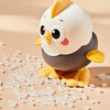A white and gray wind-up chick toy is sitting on a surface surrounded by small, clear plastic beads.