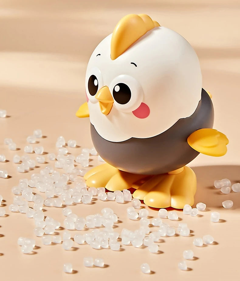 A white and gray wind-up chick toy is sitting on a surface surrounded by small, clear plastic beads.
