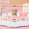 A set of pink bear cake toppers featuring a teddy bear and a pink car, displayed on a white plate.