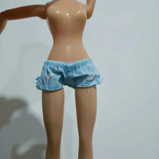 A fashion doll with light skin wearing denim shorts decorated with white floral embroidery.