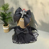 A black lace sling dress with a bow and cross detail displayed next to a potted green plant.