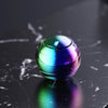 A glossy, iridescent metal fidget spinner resting on a dark, reflective surface.